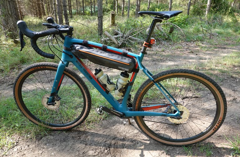 Wilier Jena in 650b mode on tan-wall WTB Venture 47 tyres, with frame bag and bottles on a pine woodland trail.