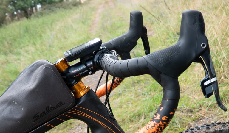 Wahoo ELEMNT ROAM ziptied to the Easton stem of a black and orange gravel bike with a Salsa frame bag.