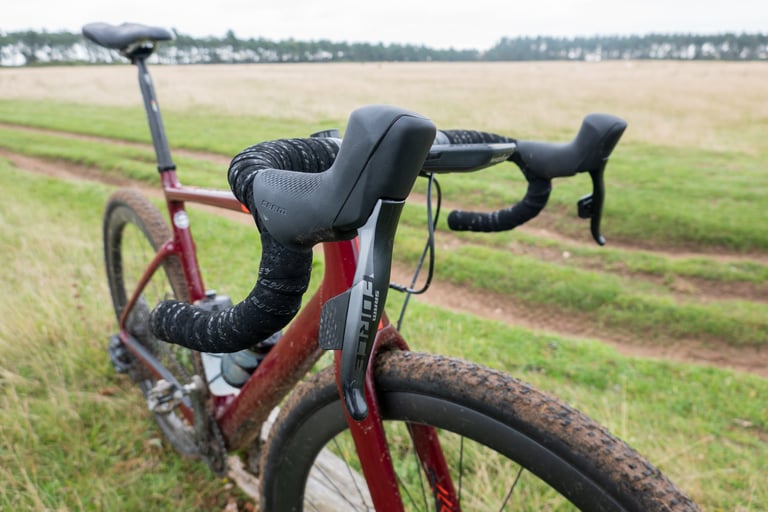 SRAM Force AXS shifter and brake lever on the drop handlebars of a red gravel bike in a field.