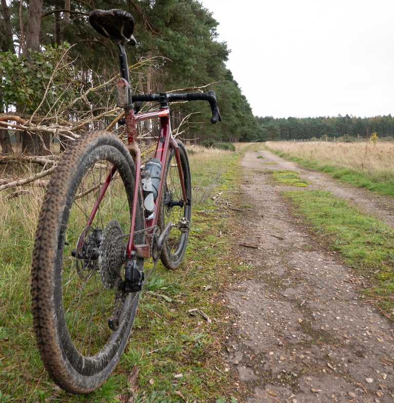 Muddy red Cervelo Aspero with a SRAM Mullet drivetrain standing beside a sandy forest track.