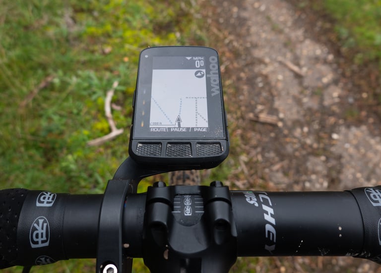 Wahoo ELEMNT ROAM showing a map with blue dashed and black trail lines, mounted on handlebars above a gravel path.