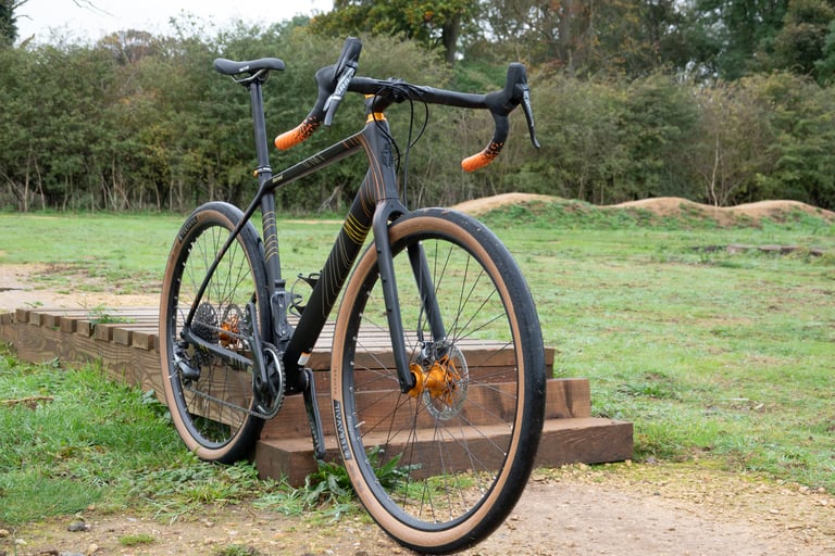Salsa Warroad Carbon Force 1 650b test bike with orange Arundel bar tape and bronze Hope hubs, standing on grass.