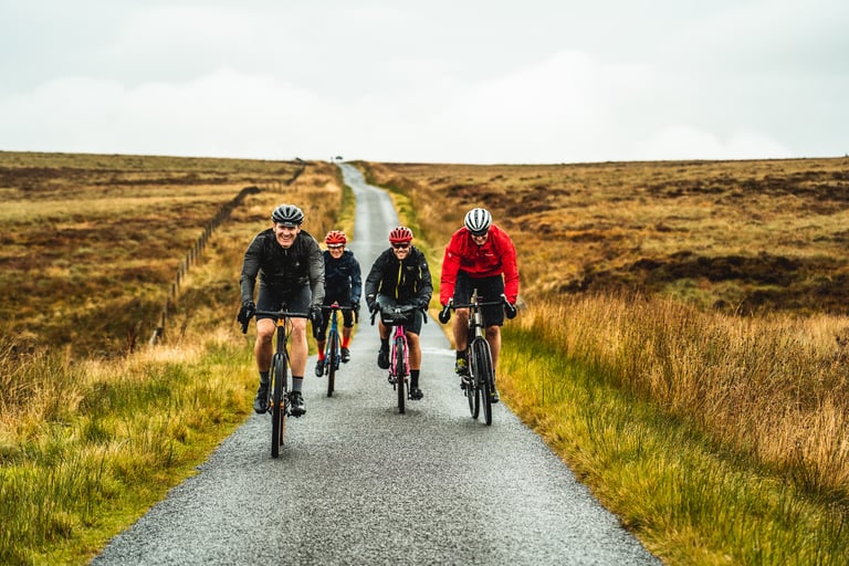 Four riders in rain jackets ride a narrow tarmac lane across open moorland on the Frontier 300 route.