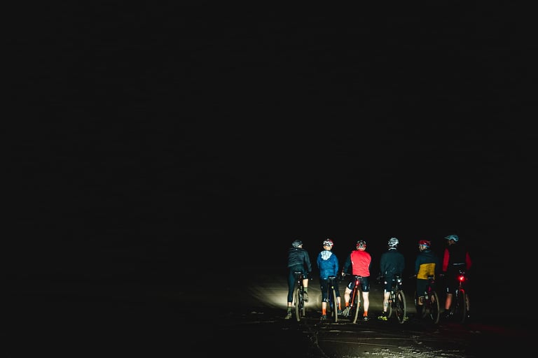 Six riders stand with their bikes in the dark on the beach at Druridge Bay, the Frontier 300 finish.