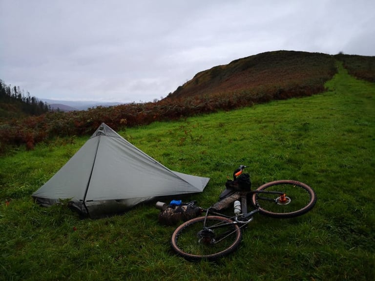 Small grey tent and a loaded bike on a bracken-edged Mid Wales hillside, the Wildcat 100 wild camp near Sennybridge.