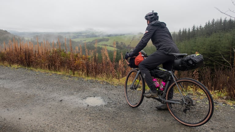 Rider on a loaded Trek Crockett pauses on a gravel forest track above a misty Mid Wales valley on the Wildcat 100.