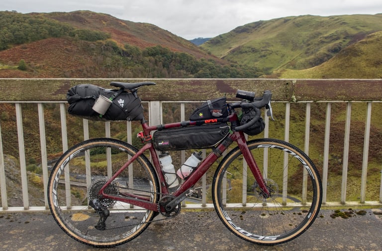 Bikepacking-loaded Cervelo Aspero with a SRAM Mullet drivetrain parked on a bridge above a green valley.