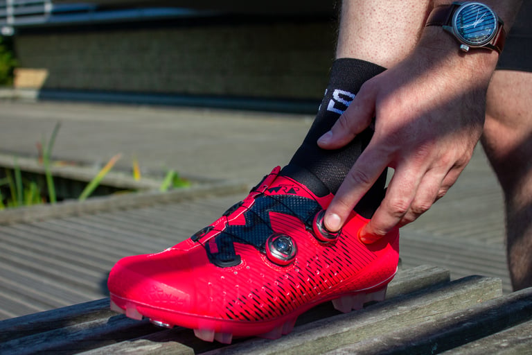 Rider turns the BOA dial on a neon red Suplest Cross Country Pro shoe to adjust the tension.