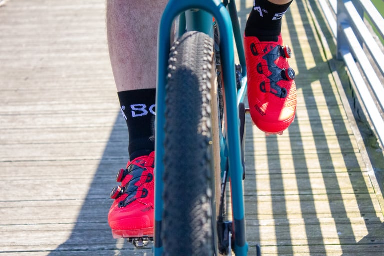 Front view of a rider's red Suplest Cross Country Pro shoes on the pedals of a teal gravel bike.