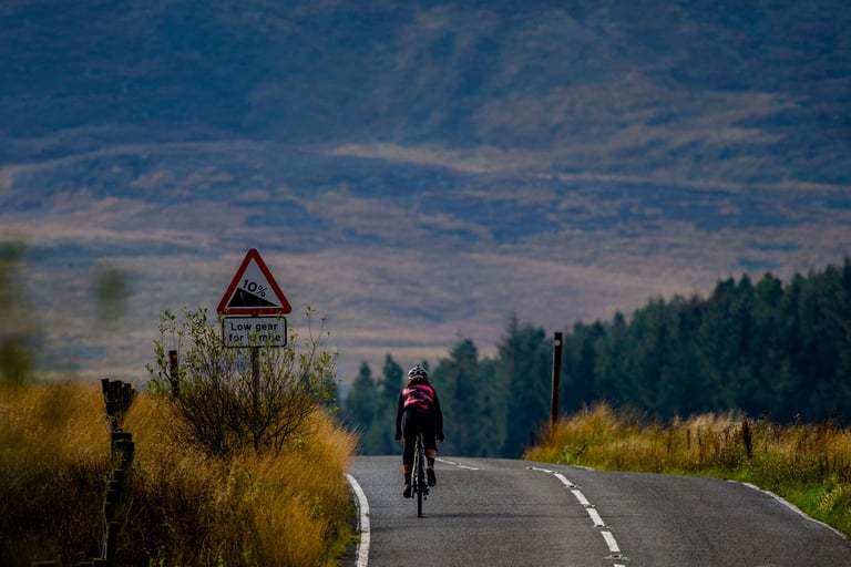 Emma Osenton rides the Tripster V3 along an empty moorland road past a 10 per cent hill sign towards a forest.