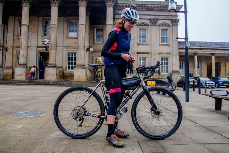 Emma Osenton pulls on her gloves beside her Kinesis Tripster V3 in front of a columned railway station.