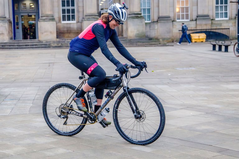 Emma Osenton rides her titanium Kinesis Tripster ATR V3 across a stone square, a frame bag on the top tube.