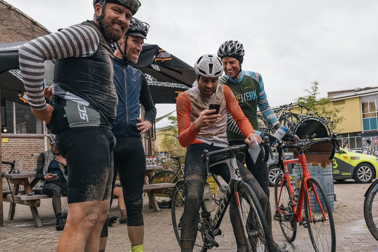 Muddy riders laugh over a phone beside their road bikes after the Scope Backyard Breakaway.