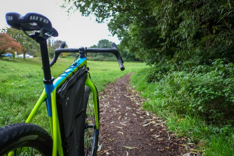 Looking over the bars of a lime green Salsa Cutthroat with frame bag, down a dirt path through a grassy meadow.
