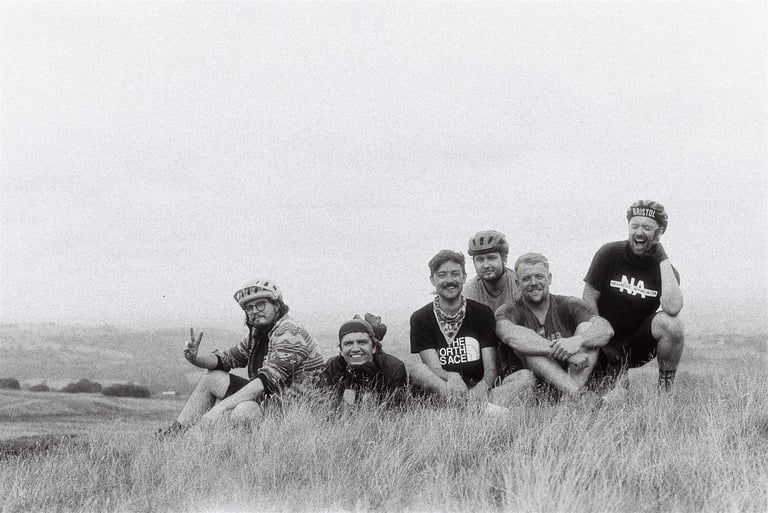 Black and white portrait of the six-strong Bristol MTB group sitting in long grass on their Skiddaw Massif loop.