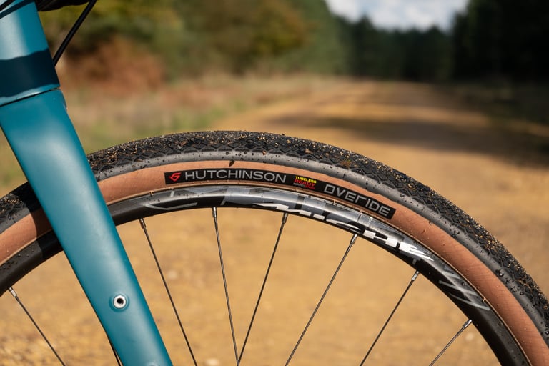 Hutchinson Overide tan-wall tyre fitted beside a teal fork on a dry gravel fireroad.