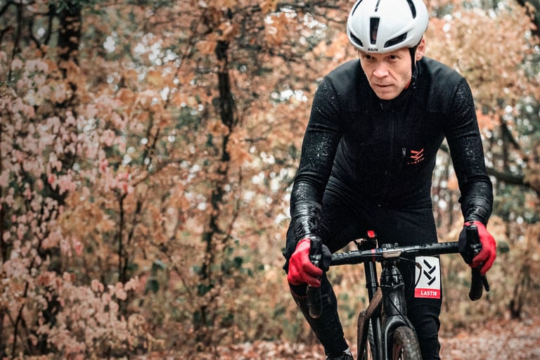 Rider in a black LASTIG cyclocross jacket and red gloves rides through wet autumn woodland.