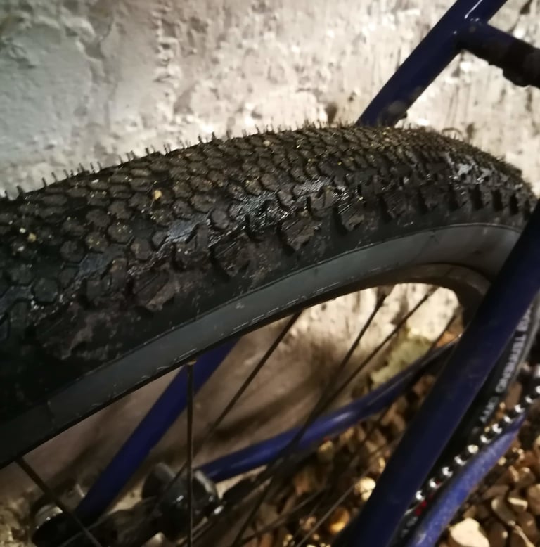 Tread of a Vittoria Terreno Dry tyre on a blue frame against a white wall, low centre knobs and larger side knobs.