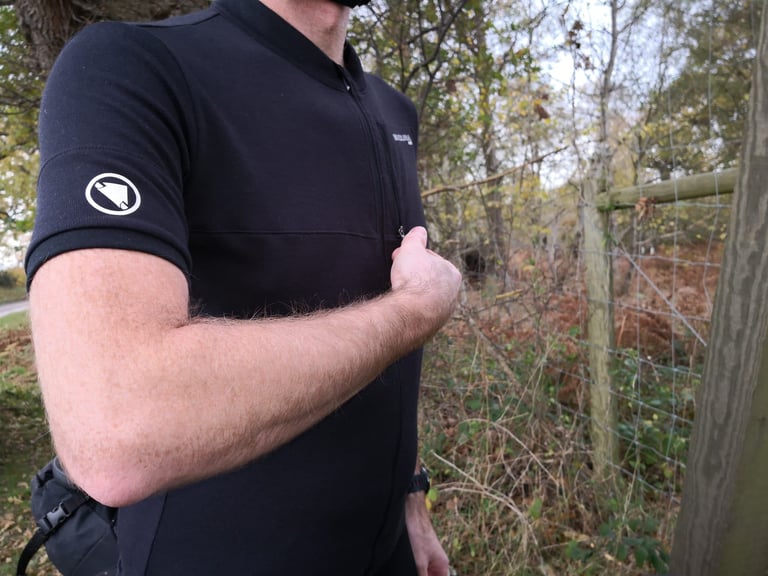Endura MTR Adventure Jersey sleeve with a circular logo and full-length chest zip, worn by a rider beside a wire fence.