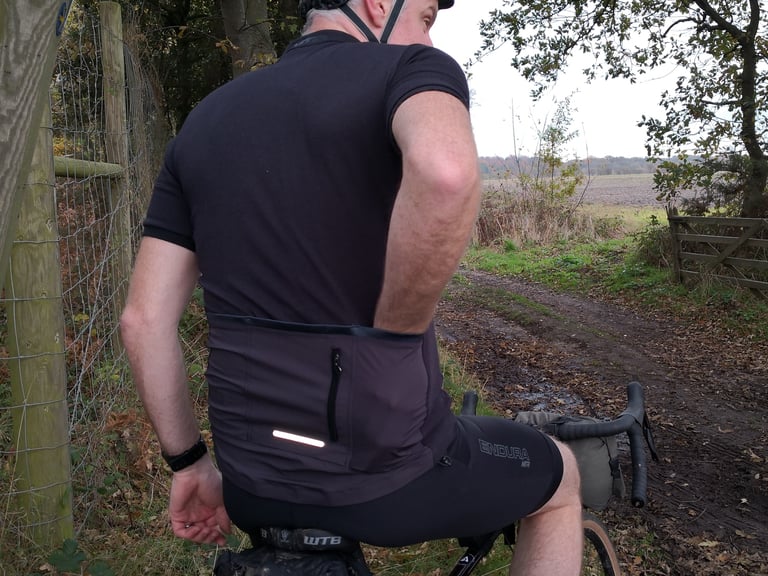 Rear of the Endura MTR Adventure Jersey with zipped pocket and reflective strip, on a rider astride a gravel bike.