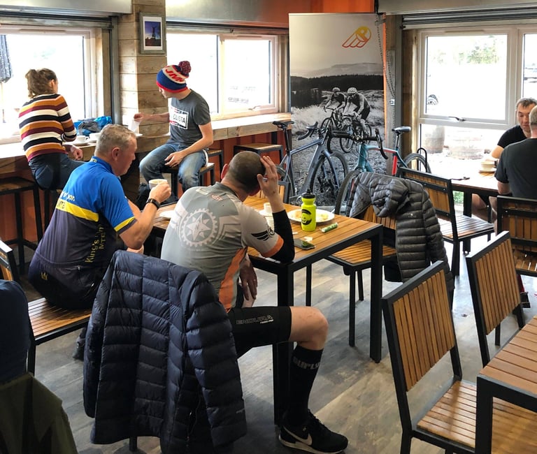 Riders in cycling kit sit at tables with coffee in the Phoenix Cycleworks cafe after the Suffolk Gravel ride.