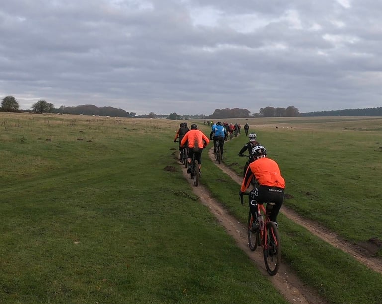 A long line of riders follows a grassy double track across open Suffolk countryside on the Phoenix Cycleworks social ride.