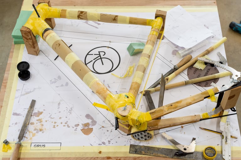 Taped bamboo tubes of the GRUS frame laid out over its full-size drawing on the Bamboo Bicycle Club bench.