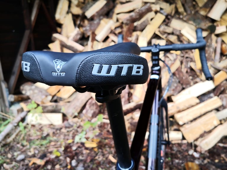 WTB Volt Sport saddle and drop bars on the Pinnacle Arkose D3, with logs stacked behind.