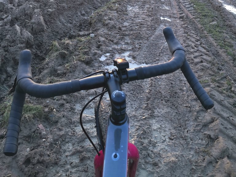 Salsa Cowchipper drop bars with black tape on the Cutthroat, shot looking down at a muddy track.