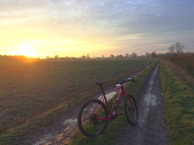 Pink Salsa Cutthroat standing on a muddy farm track at sunset, the bike being prepared for the Atlas Mountain Race.