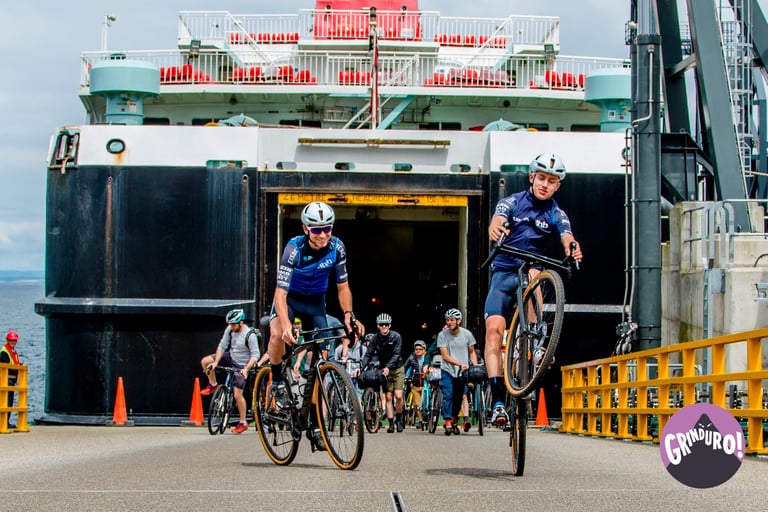 Gravel riders roll off the ferry, one pulling a wheelie, arriving for Grinduro on the Isle of Arran.