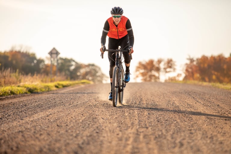 Rider in an orange gilet on a 2020 Salsa Warbird heads towards the camera down a gravel road lined with autumn trees.