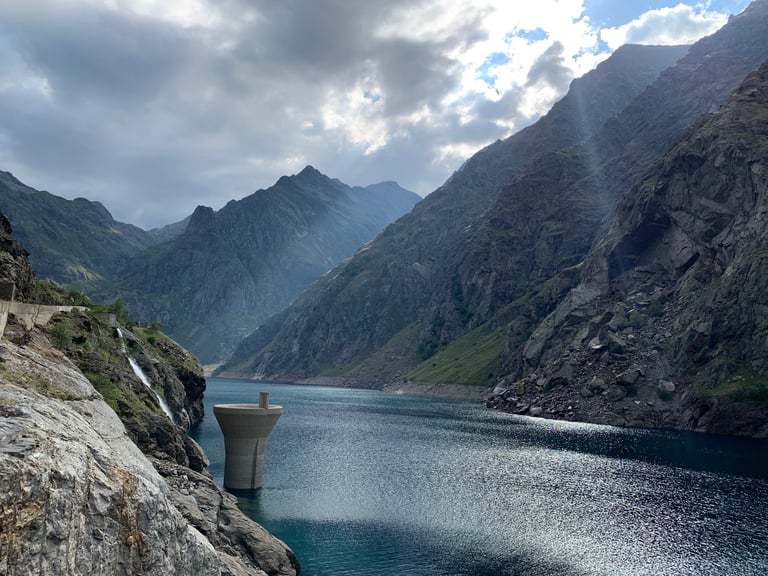 Mountain reservoir with a concrete intake tower below steep rocky slopes on the Further route in the Pyrenees.