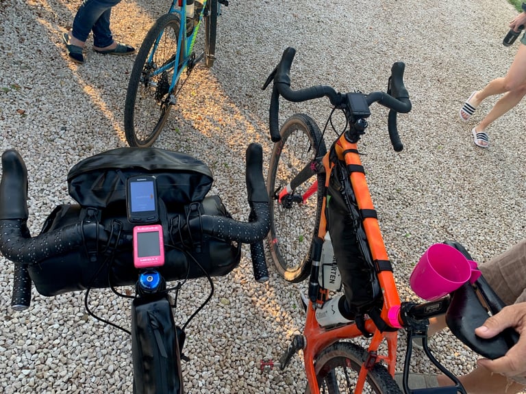 Garmin and Lezyne GPS units on a bikepacking handlebar beside an orange gravel bike at the Further race start.