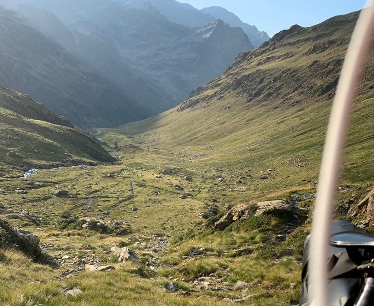 Grassy high valley with a stream and steep mountain walls, seen past a bikepacking bag on the Further route in the Pyrenees.