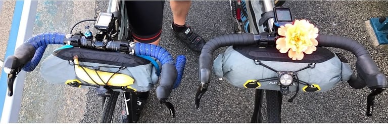 Two Apidura handlebar bags on drop bars seen from above, one with a banana tucked in, the other with a flower on top.