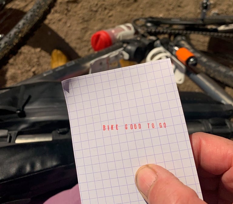 Note reading "Bike good to go" in red capitals held up over a bikepacking bike during the Further race.