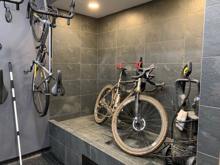 Muddy gravel bike on the slate-tiled bike wash bay at The Service Course Wilmslow, with a pressure washer beside it.