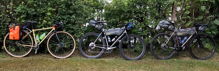 Three different bikes lined up against a hedge, each set up for bikepacking with bags and bottles.