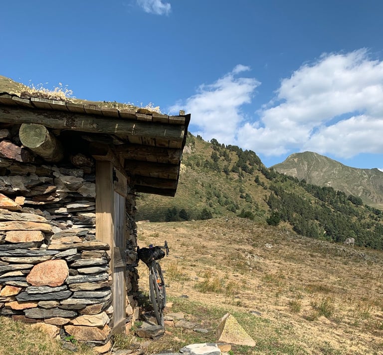 Gravel bike leaning on a stone shepherd's hut with a turf roof and a peak behind, Further route in the Pyrenees.