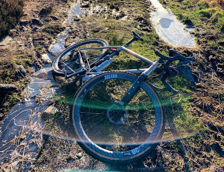Kinesis Tripster gravel bike on Sector GCi wheels lying on a frozen, muddy moorland track beside icy puddles.