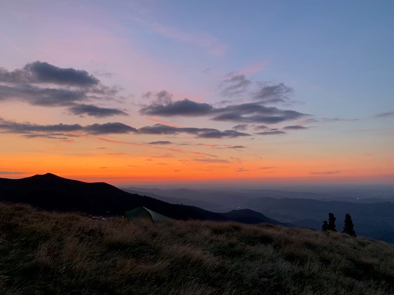 Small green bivy tent on a grassy ridge below a pink and orange sunset sky, Further race night one.
