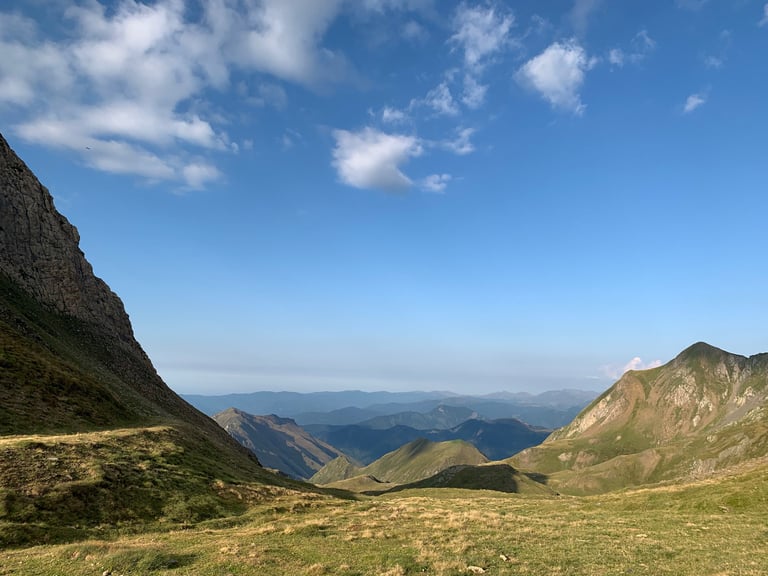 Wide mountain view across a grassy col with distant ridges on the Further route in Andorra.