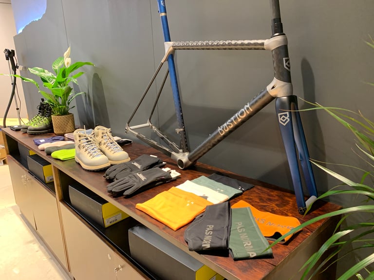 Bastion Cycles frame on display above boots, gloves and Pas Normal Studios neck warmers at The Service Course Wilmslow.