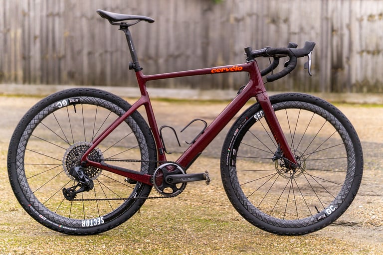 Cervelo Aspero gravel bike in dark red with Sector GCi carbon wheels and Challenge tyres, side view against a fence.