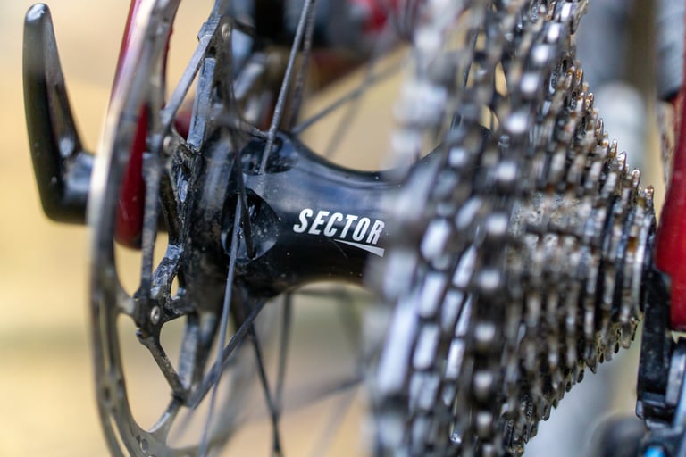 Close-up of the Sector-branded rear hub of the GCi wheelset, between the disc rotor and a muddy cassette.
