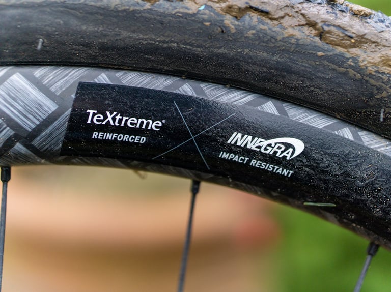 Close-up of the Sector GCi rim decal reading TeXtreme Reinforced and Innegra Impact Resistant, beside a muddy tyre.