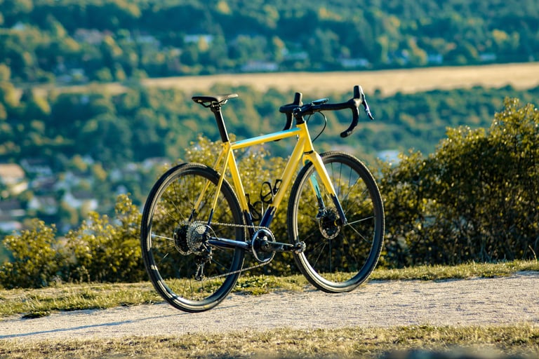 Wish One SUB gravel bike in yellow, rear three-quarter view on a hilltop track above a wooded valley.