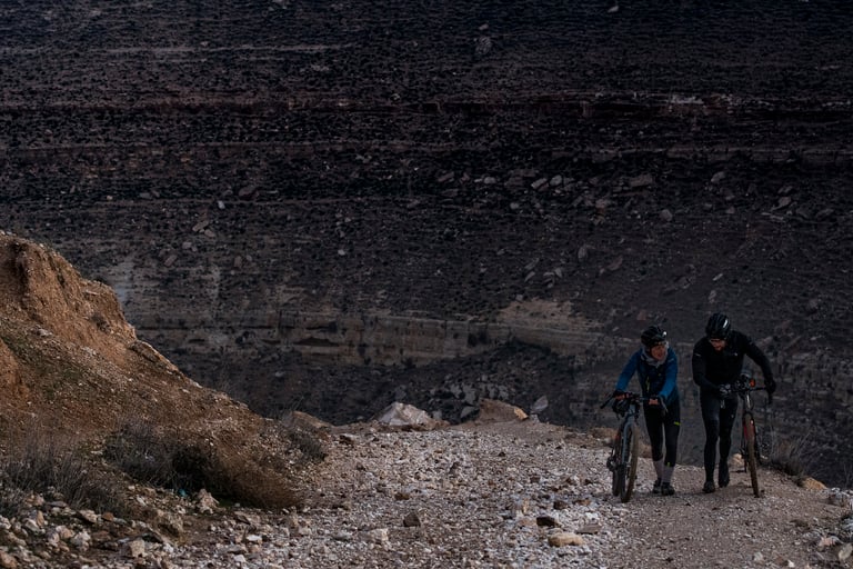 Axel and Jonas push their bikes up a stony track below dark layered rock on the Jordan Bike Trail.