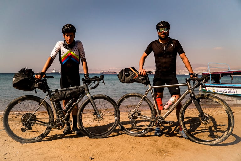 Axel Carion and Jonas Deichmann stand with their loaded gravel bikes on the Red Sea shore after crossing Jordan.